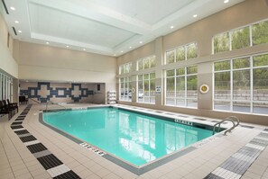 Une piscine intérieure avec des lignes de démarcation bien visibles, un sol carrelé et une vue sur l’extérieur grâce à de grandes fenêtres.