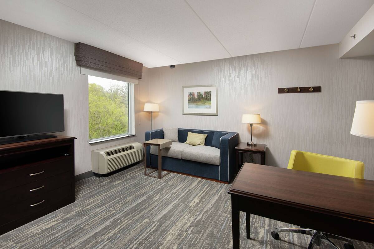 A hotel room with a flat-screen TV, a sofa, a dining table, and a chair.