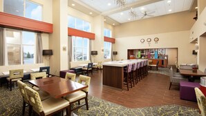 Um amplo hall de hotel com uma ilha central, diversas áreas de estar e uma kitchenette.