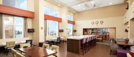 A spacious hotel lobby with a central island, multiple seating areas, and a kitchenette.