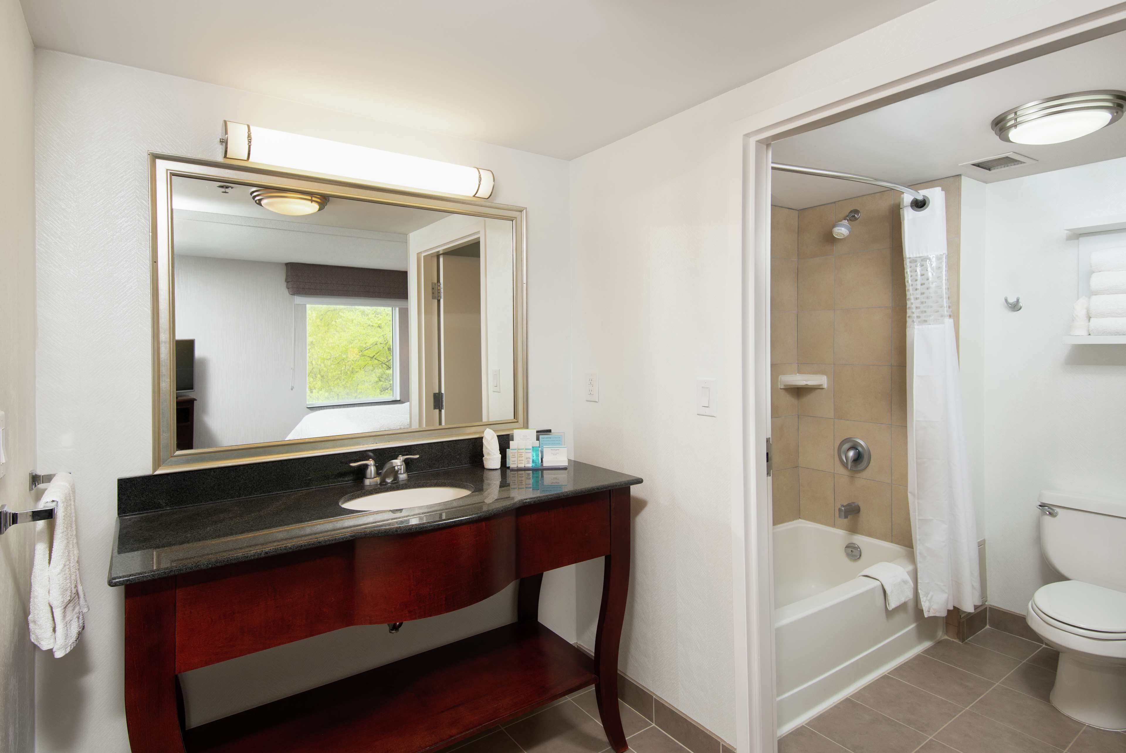 A bathroom with a dark wood vanity, a large mirror, a white sink, and a shower area.