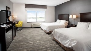 Quarto de hotel com duas camas, uma escrivaninha com cadeira, televisão e janela com vista.