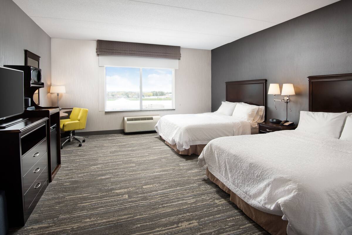 A hotel room with two beds, a desk with a chair, a television, and a window with a view.