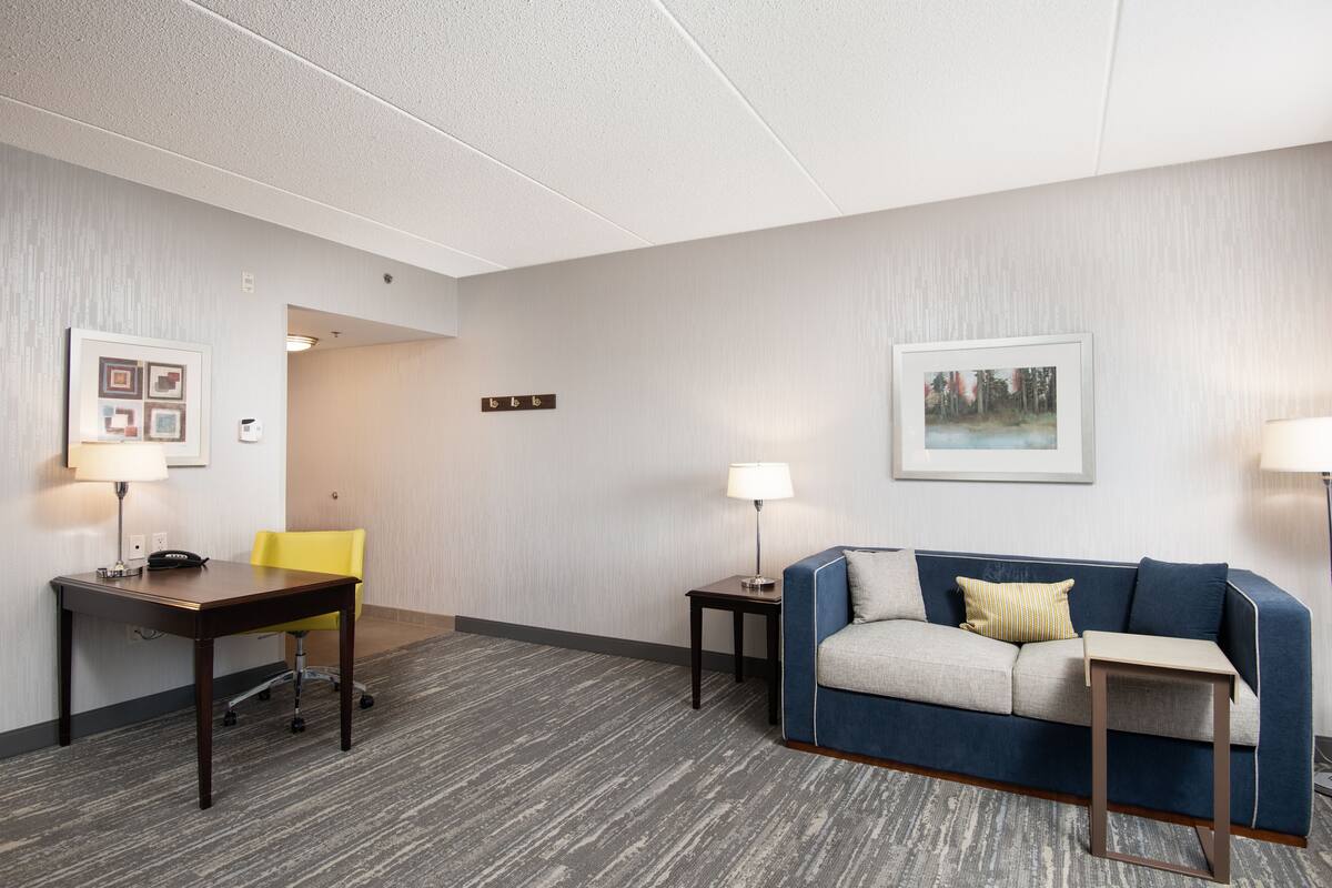 A hotel room with a desk, a yellow chair, a blue sofa, and a small table.