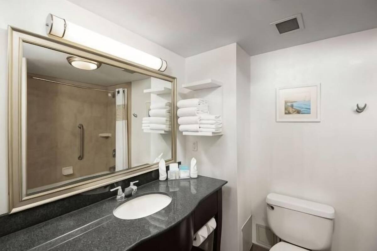 A bathroom with a sink, mirror, toilet, and towel rack.