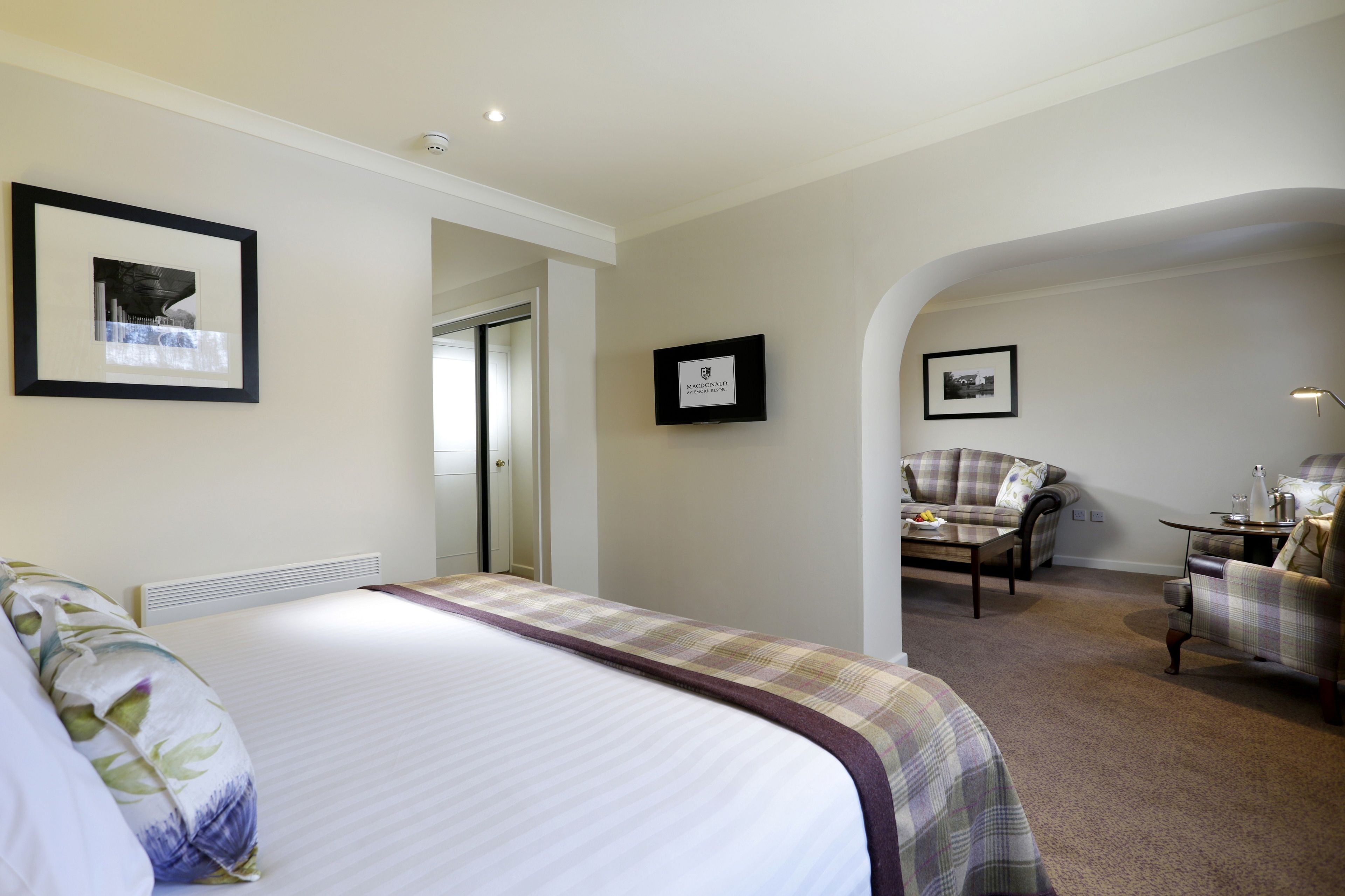 Une chambre d’hôtel avec un grand lit, une chaise, une petite table et des tableaux encadrés aux murs.
