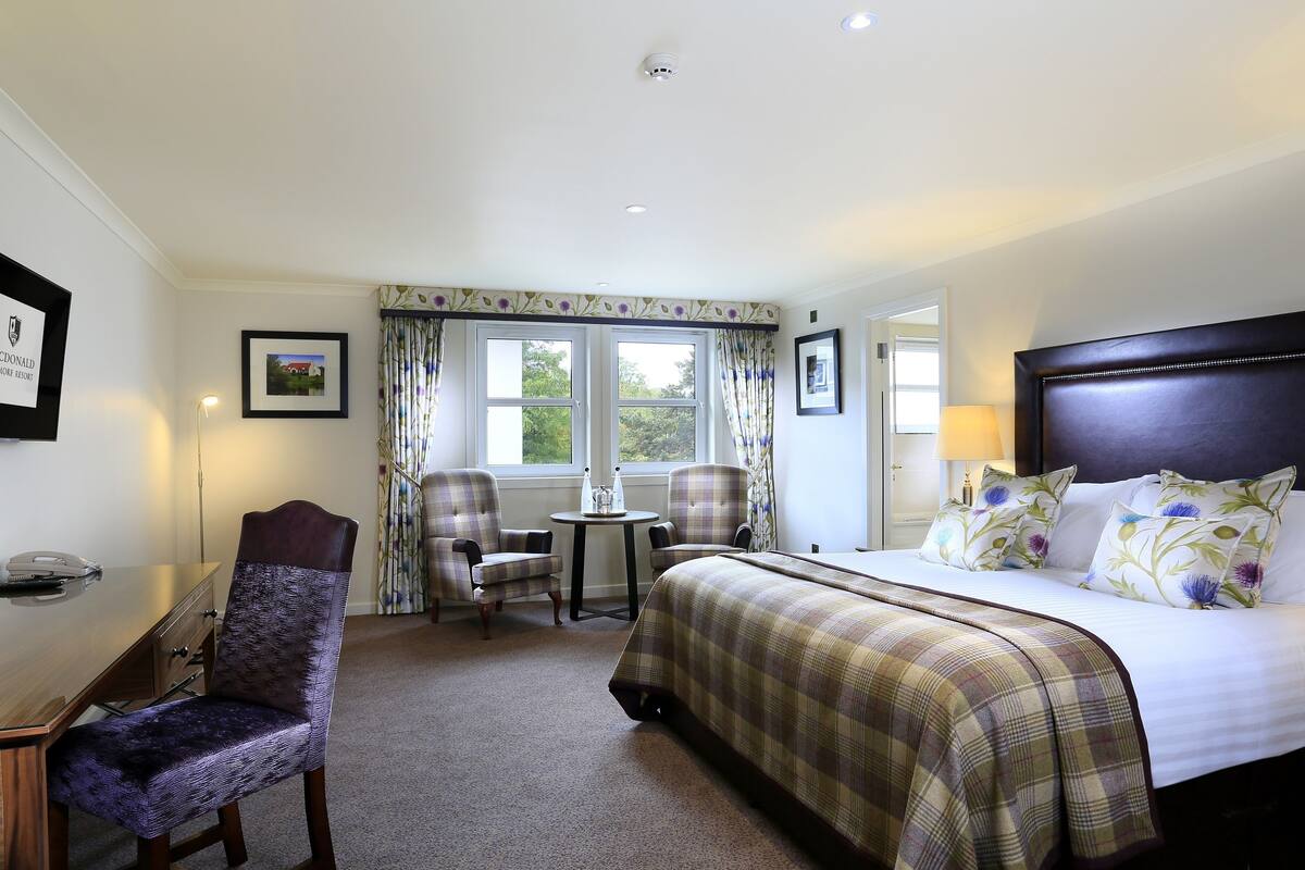 A hotel room with a bed, a desk, a chair, and a window with curtains.
