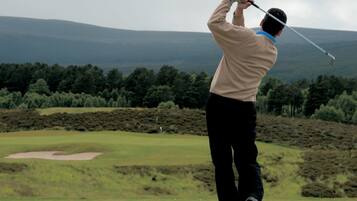 A person playing golf on a course with a view of distant hills and trees.