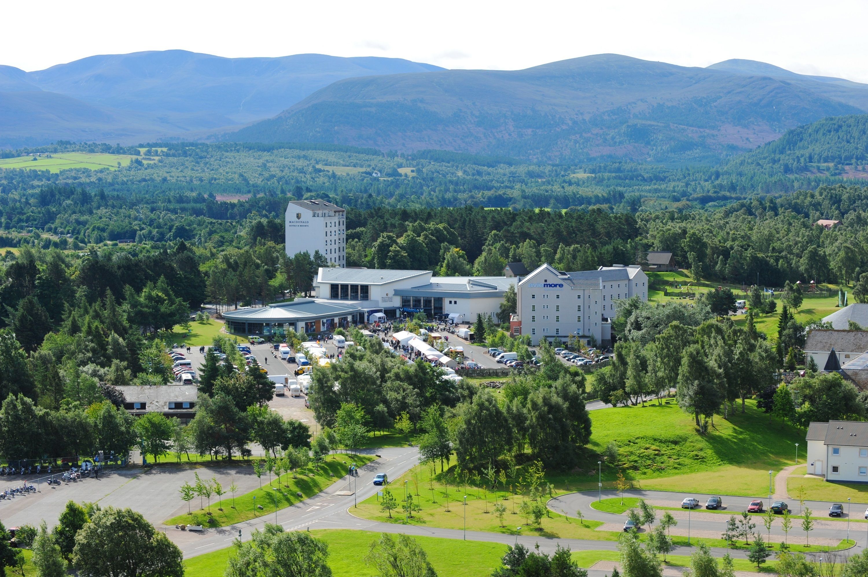 A large hotel with multiple buildings, surrounded by lush greenery and mountains in the background.