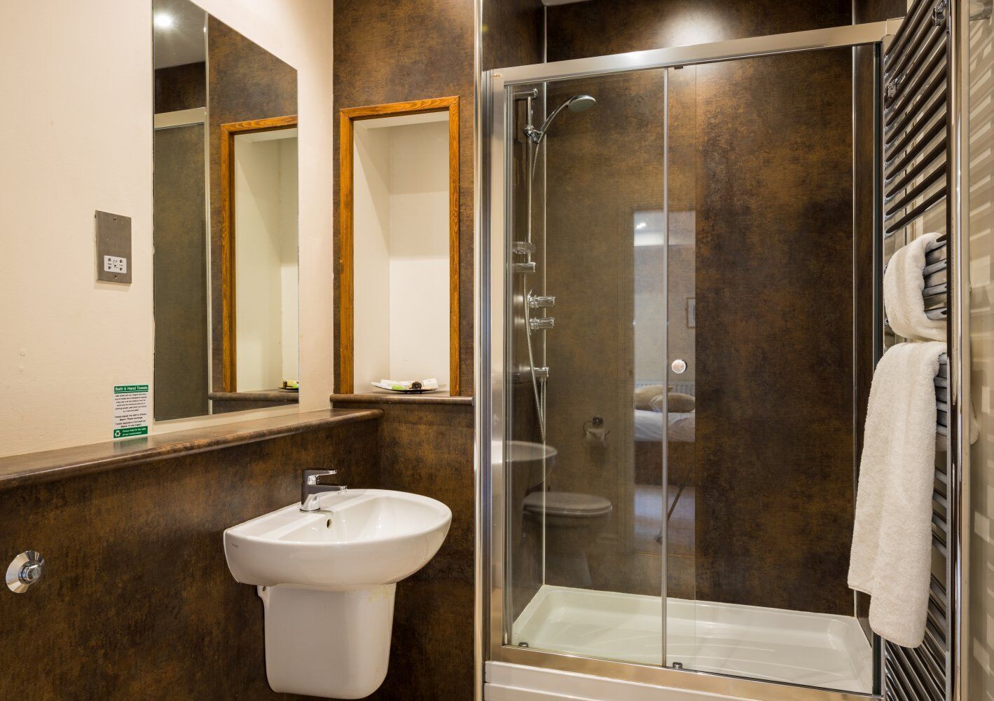 Un baño moderno con ducha de vidrio, un lavabo blanco y dos espejos.