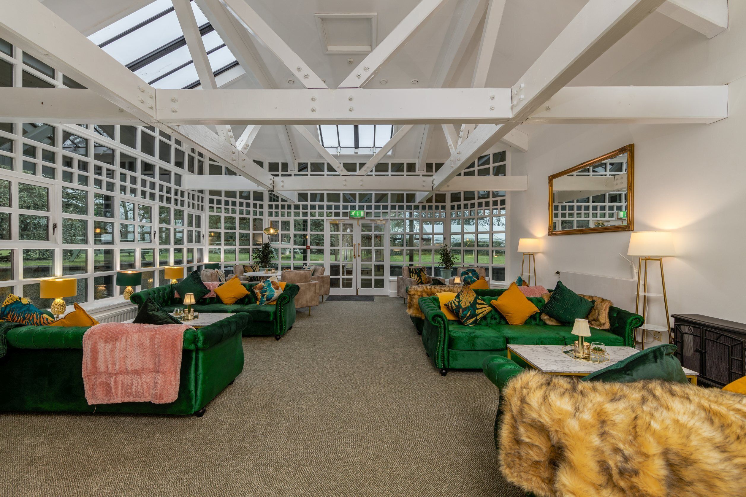 Ein geräumiges Zimmer mit grünen Sofas, einem Fellüberwurf und einem großen Spiegel.