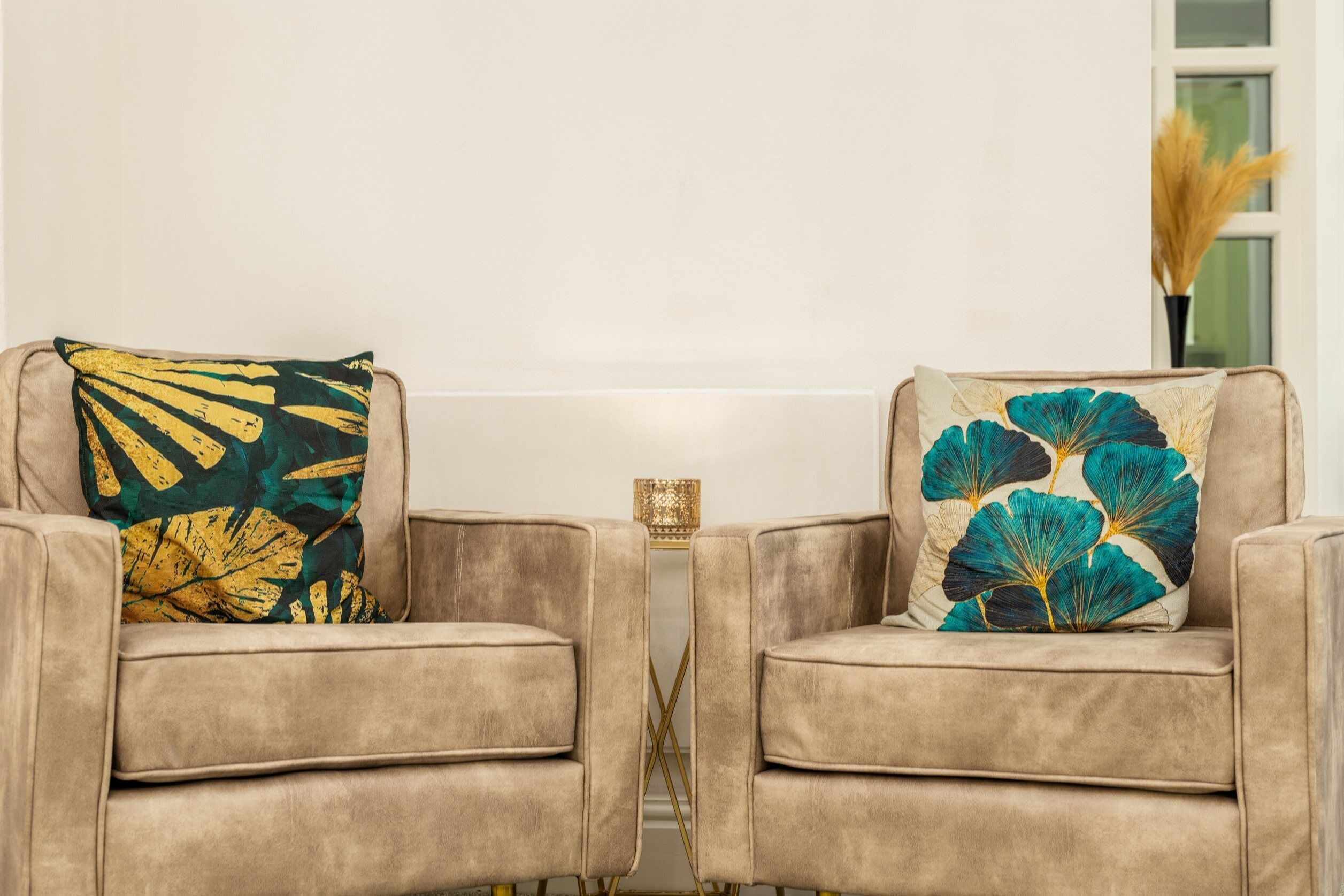 Two armchairs with floral cushions, a small side table, and a vase with dried plants.