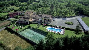 Una extensa propiedad con varias construcciones, cancha de tenis, piscina y zona de estacionamiento.