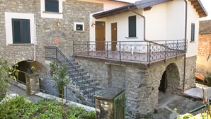 Un edificio de piedra con balcón, escaleras y un pequeño jardín.