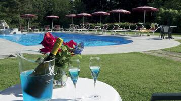 Escena junto a la piscina con sillas de descanso, sombrillas y una mesa con una bebida y flores.