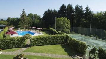 Pista de tenis, piscina y zona de estar cubierta con sombrillas.