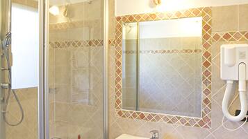 Un baño con ducha compartimentada con vidrio, un lavamanos y un espejo con un detalle de azulejos decorativos.