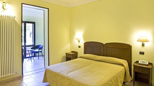 A hotel room with a bed, bedside lamps, a nightstand, and a chair in the adjacent room. - Park Hotel La Pineta (Mulazzo)