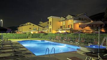 Una piscina con sillones de playa y sombrillas, rodeada de edificios con balcones y terrazas.