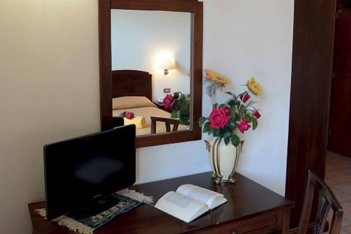 A desk with a television, a mirror, a vase with flowers, and a lamp.