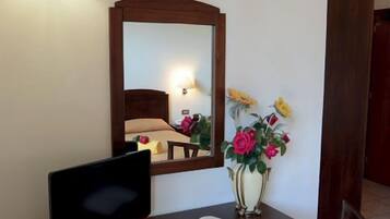 Una scrivania con televisione, uno specchio, un vaso con fiori e una lampada.