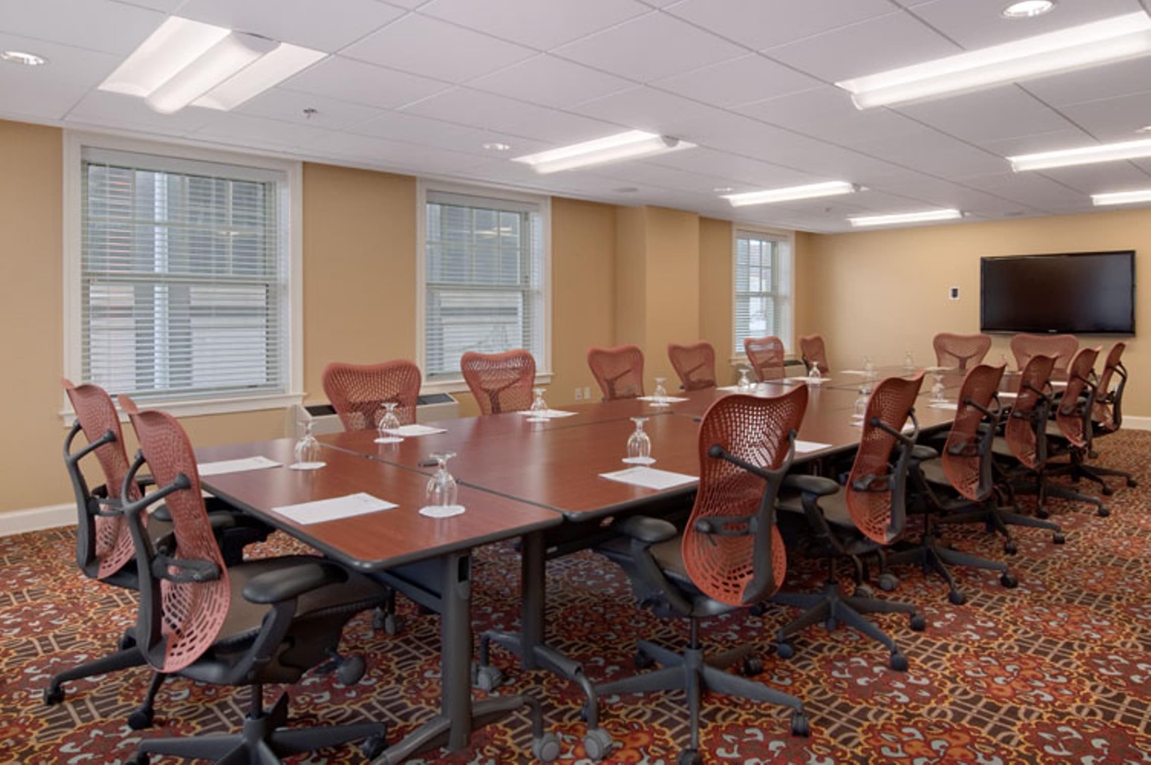 A conference room with a long table, multiple chairs, and a flat-screen TV on the wall.