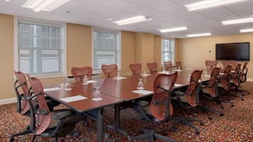 A conference room with a long table, multiple chairs, and a flat-screen TV on the wall.