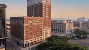 A tall red brick building with a flat roof, surrounded by other buildings and a bridge in the background. - DoubleTree Suites by Hilton Hotel Detroit Downtown - Fort Shelby (Detroit)