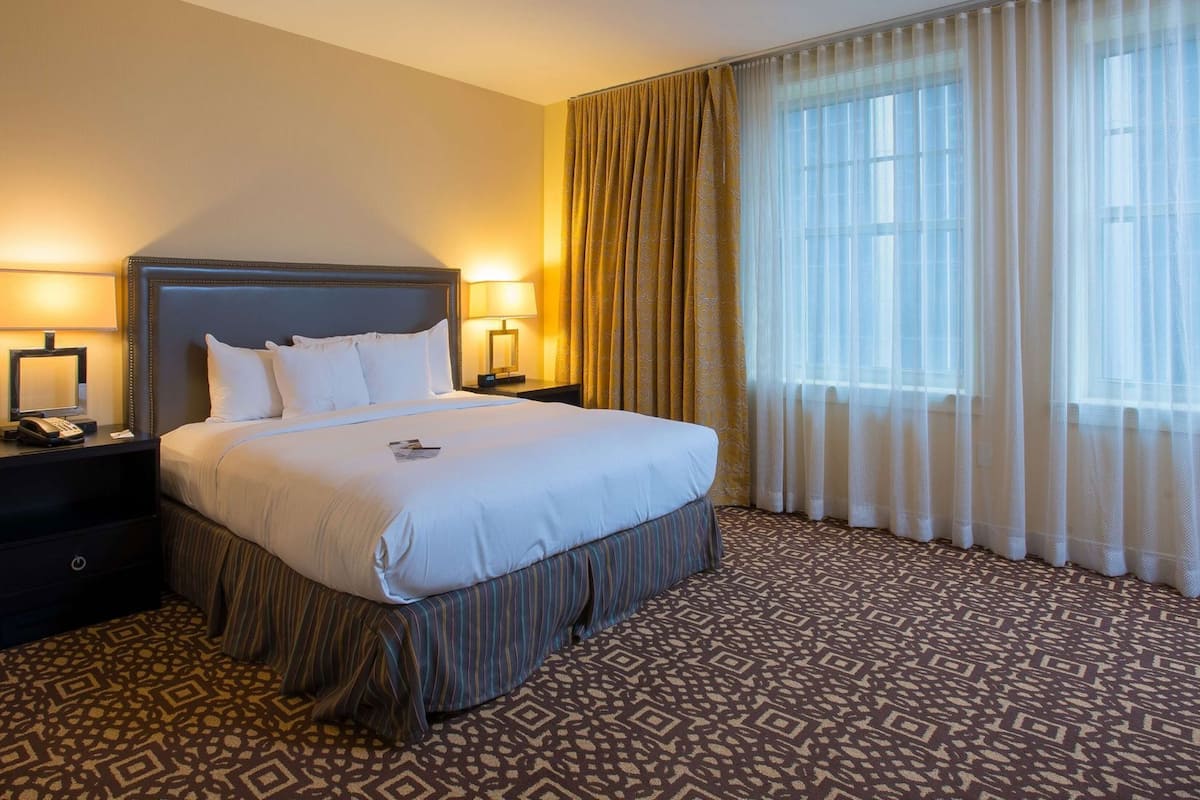 A hotel room with a large bed, two bedside tables with lamps, a telephone, and a patterned carpet.