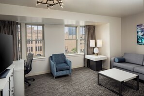 A hotel room with a desk, two chairs, a sofa, a coffee table, and a TV. - DoubleTree Suites by Hilton Hotel Detroit Downtown - Fort Shelby (Detroit)