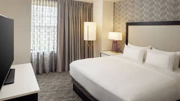 Une chambre d’hôtel avec un grand lit, un bureau doté d’un téléviseur à écran plat, une lampe et une fenêtre avec des rideaux.