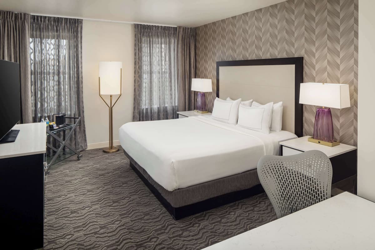 A hotel room with a large bed, two bedside tables with lamps, a desk, and a chair.