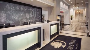 A hotel reception area with a modern design, featuring a reception desk, a chalkboard with technical drawings, and a carpet with the hotel name. - DoubleTree Suites by Hilton Hotel Detroit Downtown - Fort Shelby (Detroit)