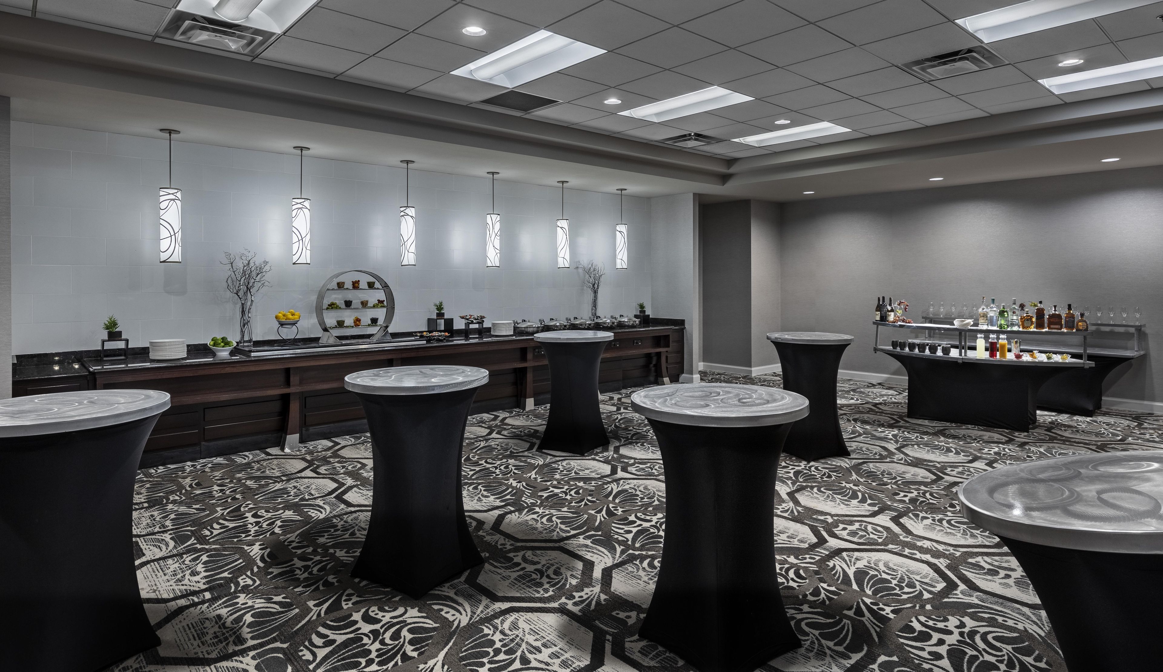 A modern bar area with round tables, a long counter, and a bar stocked with various bottles.