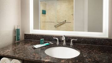 Un baño con encimera de granito, un lavabo blanco y un espejo grande que refleja la zona de la ducha.