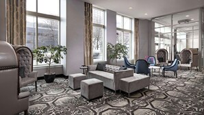 A modern hotel lobby with a seating area featuring a sofa, chairs, and a small table. There are large windows providing views of the outside. - DoubleTree Suites by Hilton Hotel Detroit Downtown - Fort Shelby (Detroit)