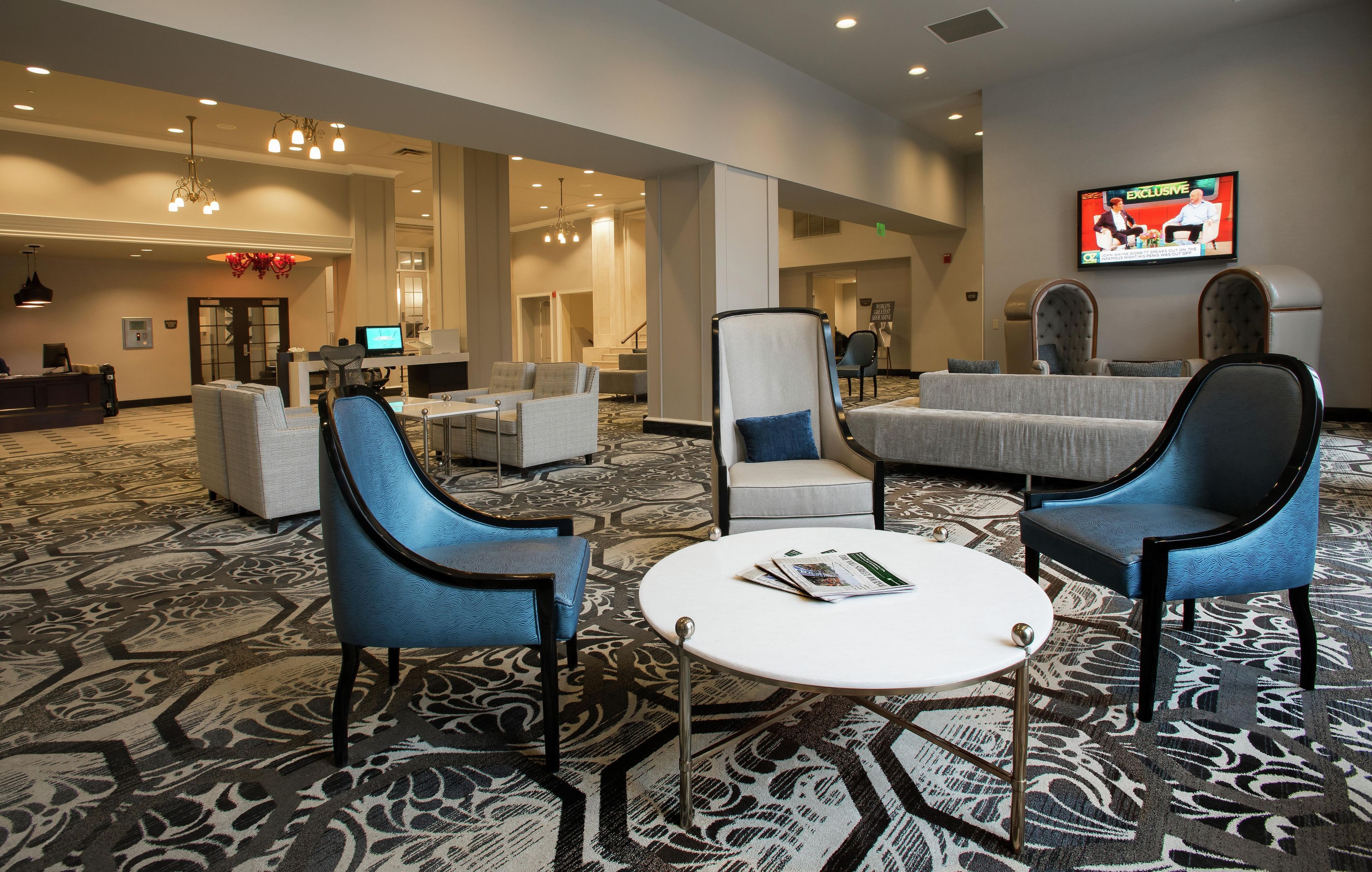 A hotel lobby with a reception desk, seating area, and a television screen displaying a news program.