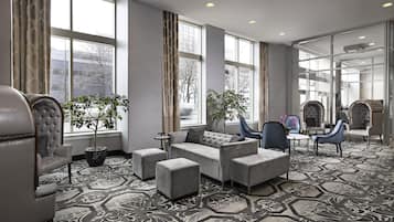 Un vestíbulo de hotel con zona de estar, ventanas amplias y alfombra estampada.