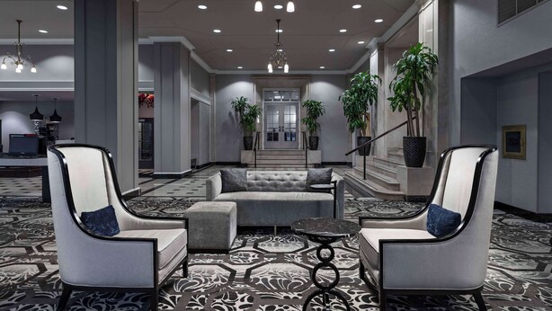 A modern hotel lobby with a sofa, two armchairs, a coffee table, and potted plants. - DoubleTree Suites by Hilton Hotel Detroit Downtown - Fort Shelby (Detroit)