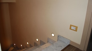 Una escalera con barandilla de mármol y una lámpara fijada a la pared.
