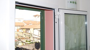 Una habitación con puerta corrediza de vidrio que da a un balcón, techo blanco con una lámpara y una ventana con cortina.