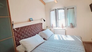 Un dormitorio con cama, vigas de madera en el techo, una ventana con cortinas y una mesita de noche con lámpara.