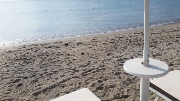 Una playa con huellas en la arena, un paraguas blanco y una silla de descanso blanca.