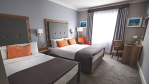 Habitación de hotel con dos camas, un escritorio, una silla y un ventanal con cortinas.