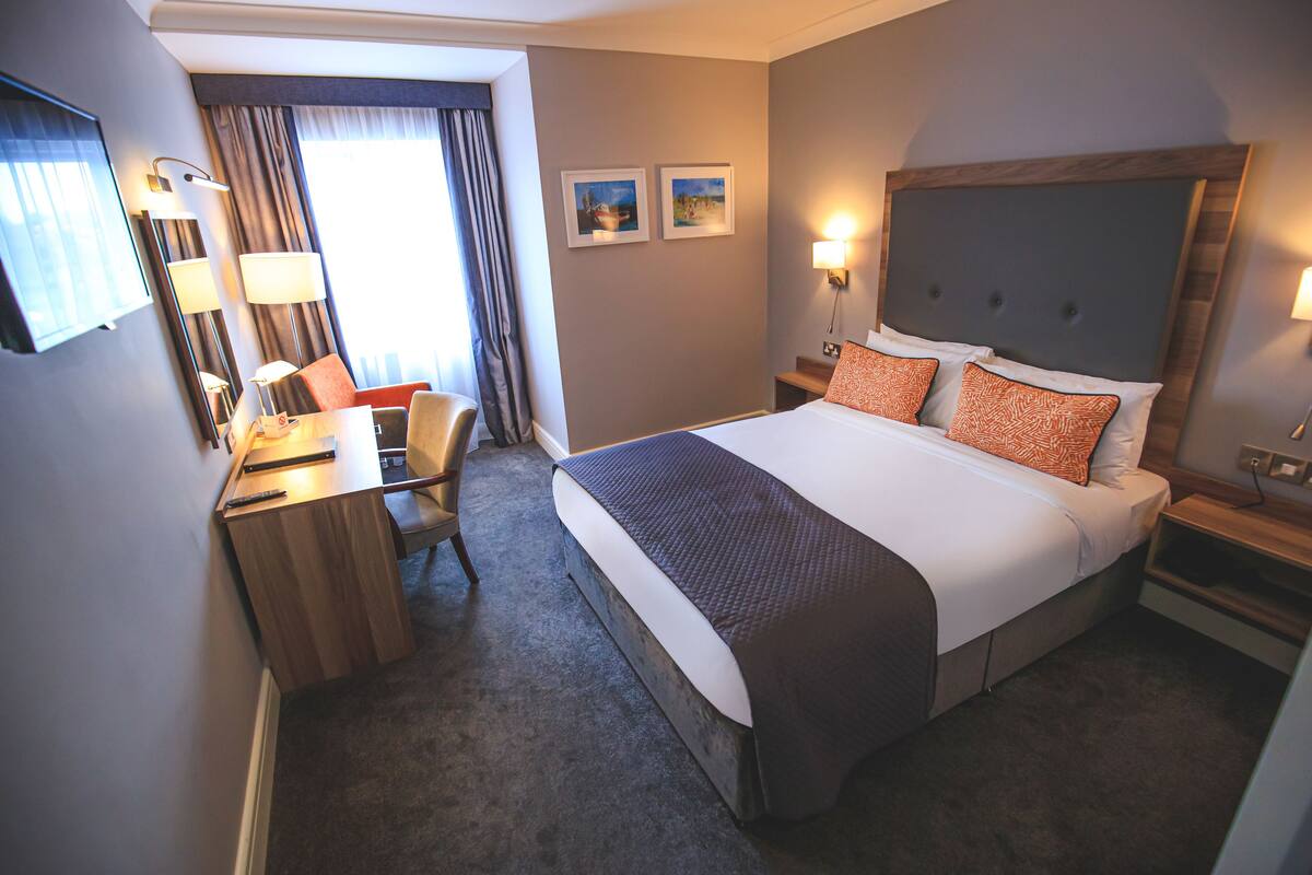 A hotel room with a large bed, a desk, a chair, and a nightstand.