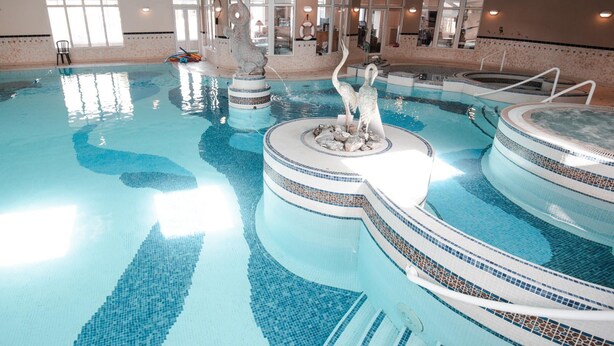Una amplia piscina interior con varios niveles y una escultura de fuente central.