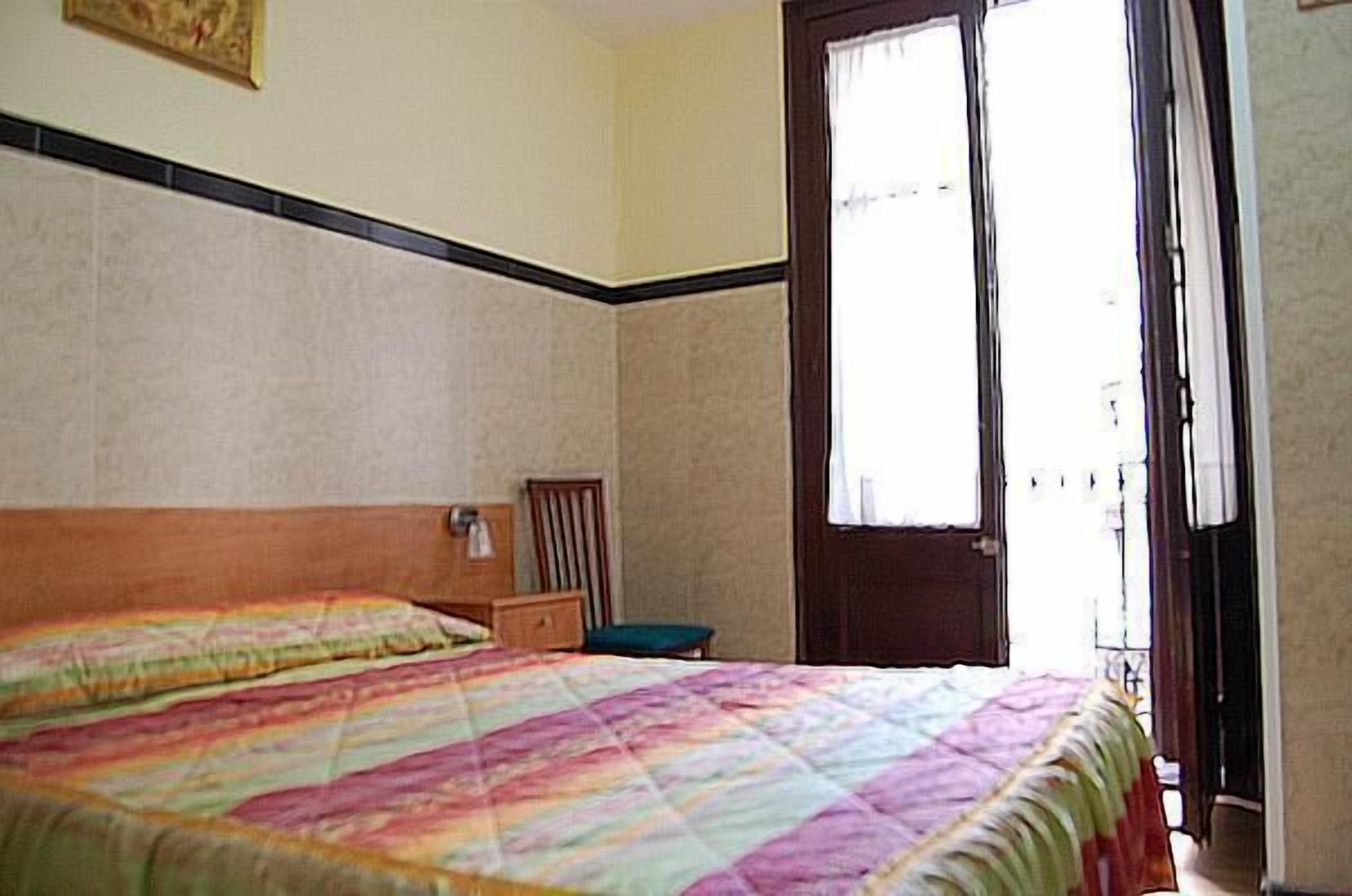 Ein Schlafzimmer mit einem Bett, einem Sessel, einem Nachttisch und einem Fenster mit Vorhängen.