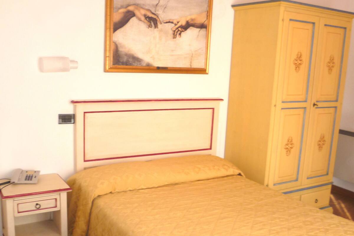 A bedroom with a bed, a nightstand with a telephone, a wardrobe, and a painting on the wall.