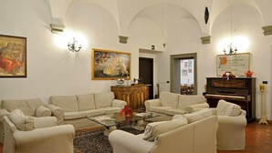 A living room with a piano, sofas, a glass coffee table, and a painting on the wall. - Hotel Vasari (Florence)