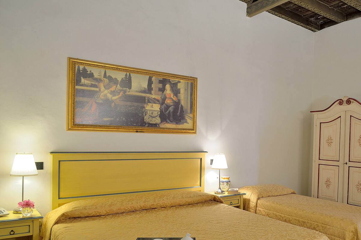 A hotel room with a large bed, two bedside tables, a nightstand, a lamp, a painting on the wall, and a wardrobe.